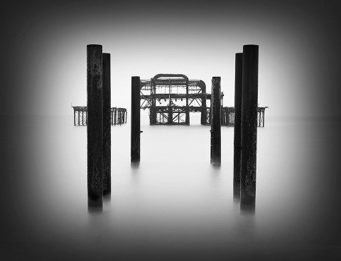 Seascape long exposure old derelict Brighton Pier in England in the Ocean in black and white looking towards the metal structure low key