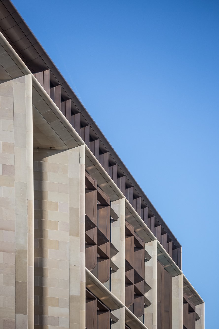 Pale stone colonnade receding diagonally against a blue sky.