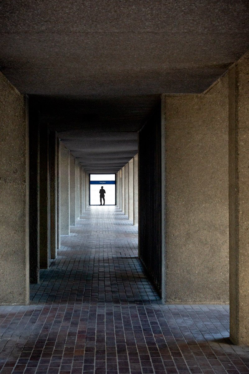 Lone figure framed at the end of a repeating concrete colonnade.