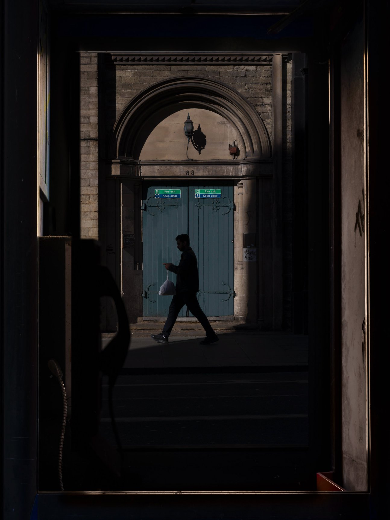 Silhouetted pedestrian framed by a stone archway and pale blue doors.