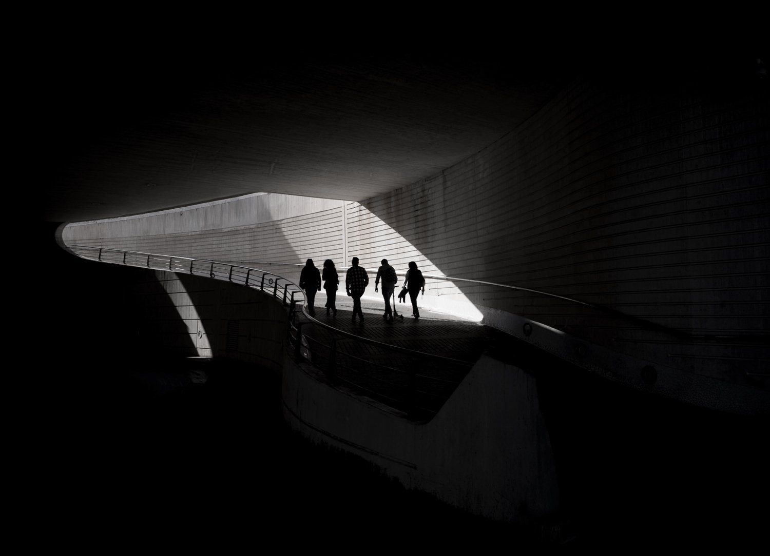 Five figures silhouetted at the bright end of a curved pedestrian tunnel.