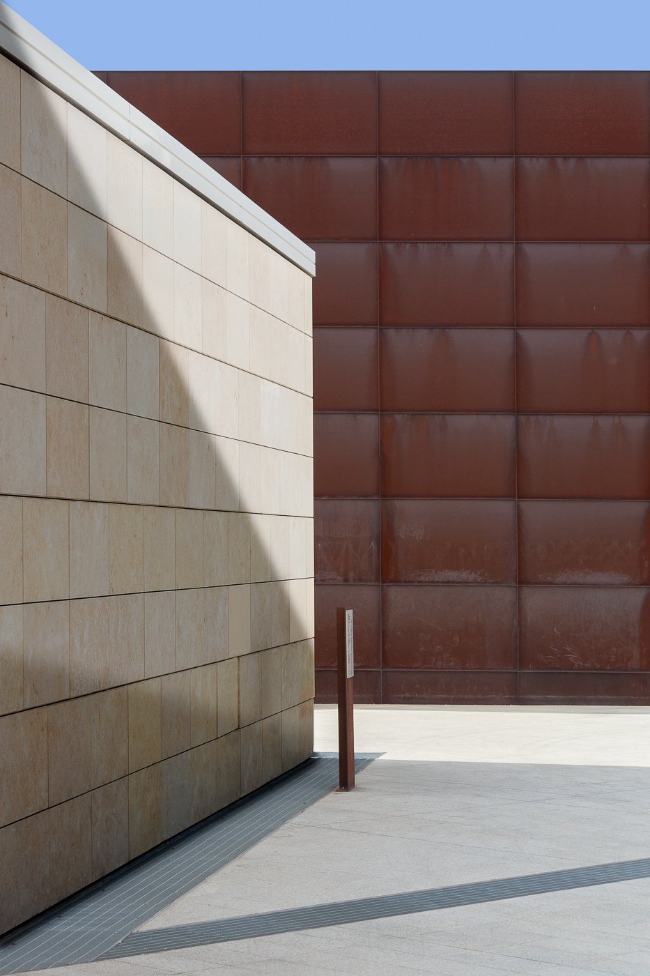 Minimal beige and rust-red walls divided by a sharp diagonal shadow.