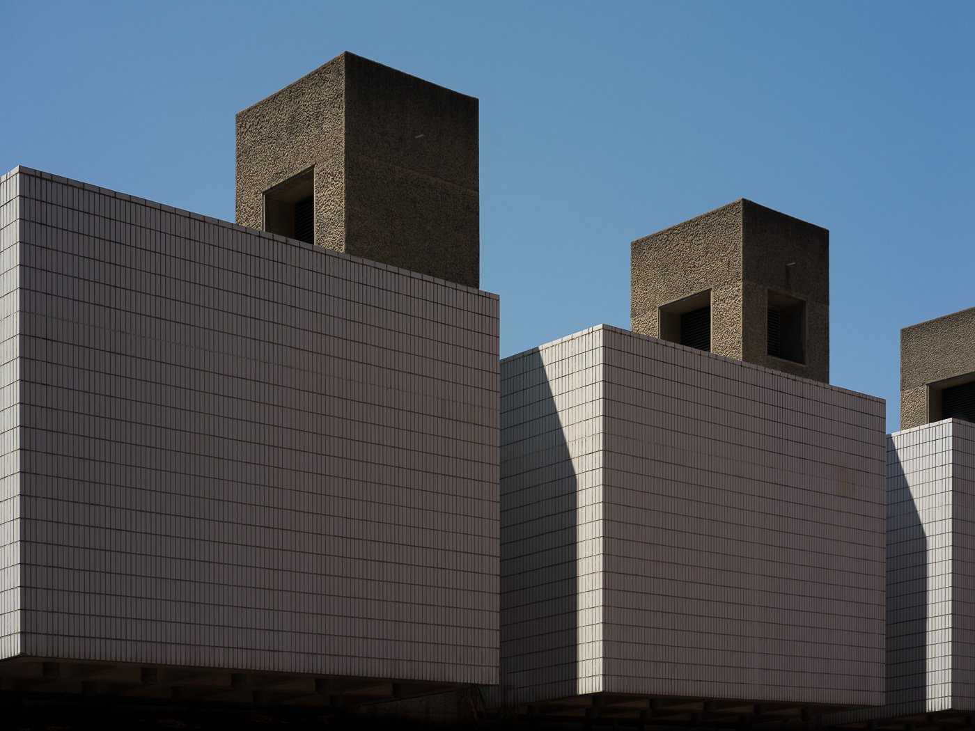 Dark block-like architectural forms against a clear blue sky.