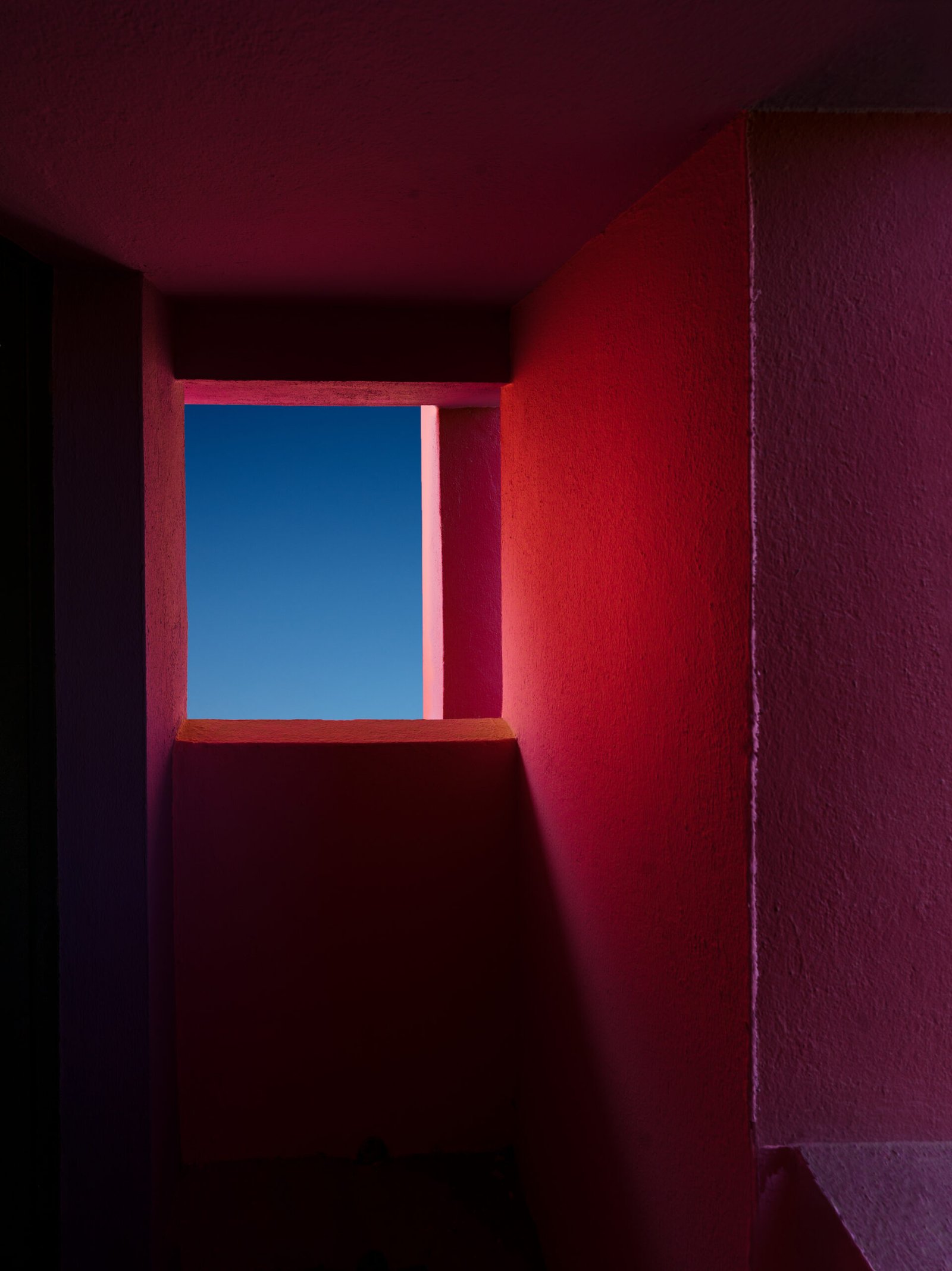 Deep red architectural opening framing a square of blue sky.