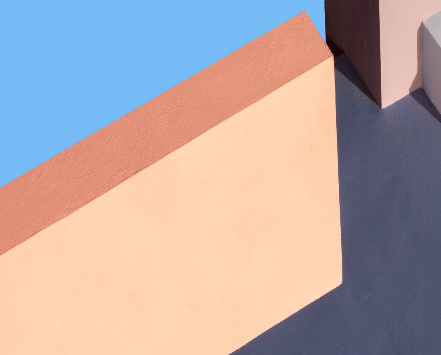 Peach and terracotta architectural planes forming a sharp diagonal against blue sky.