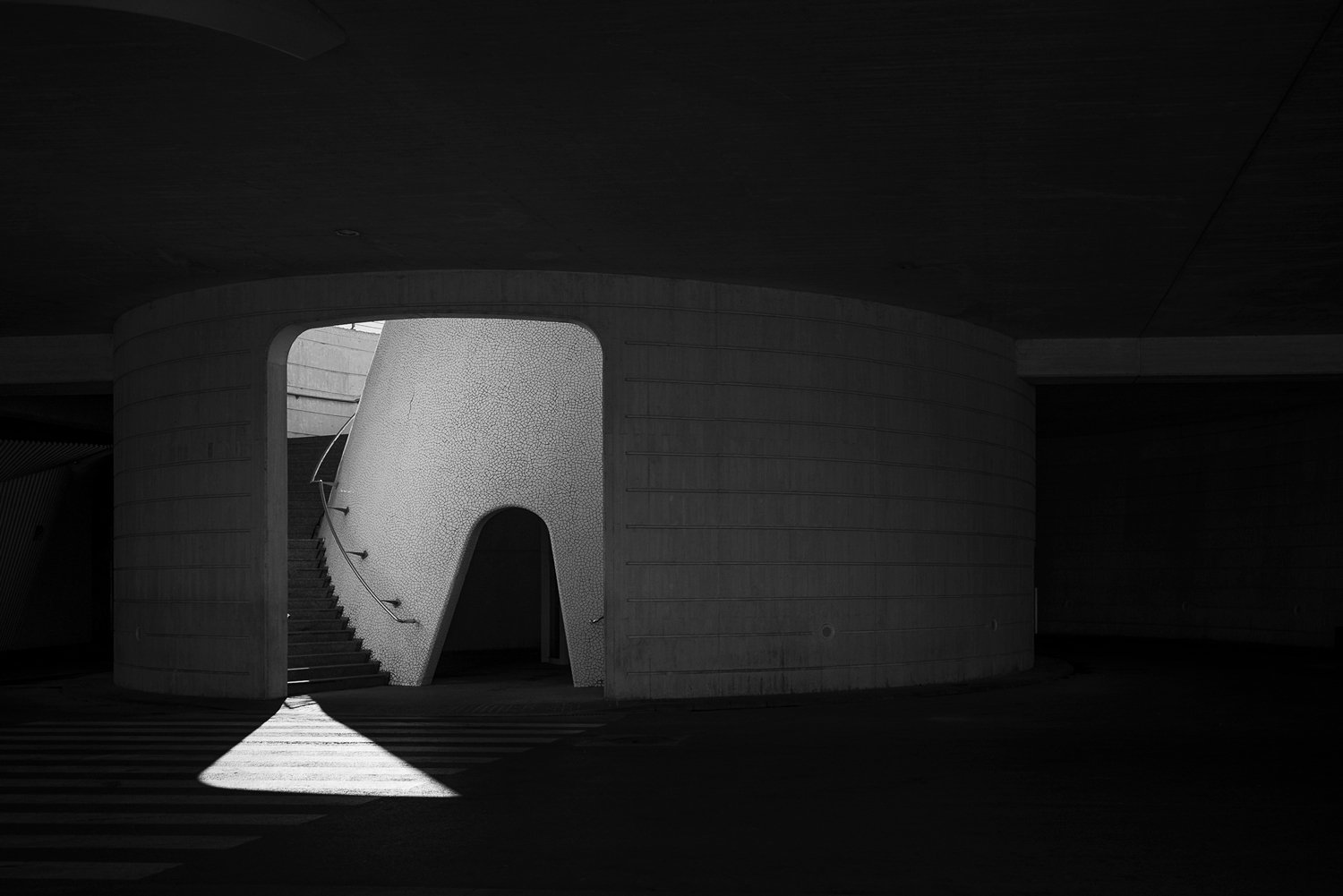 Black-and-white architectural study of a pale cylindrical form framed by deep shadow.