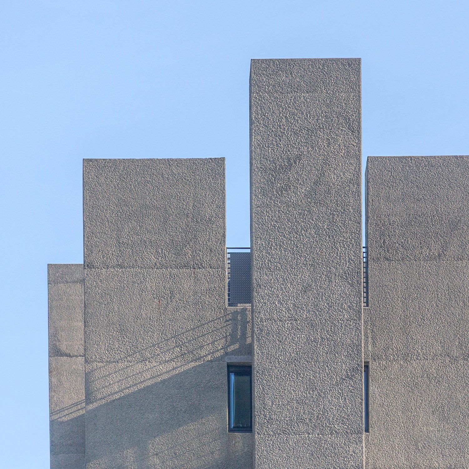 Three grey rectangular architectural blocks rising against a clear blue sky.