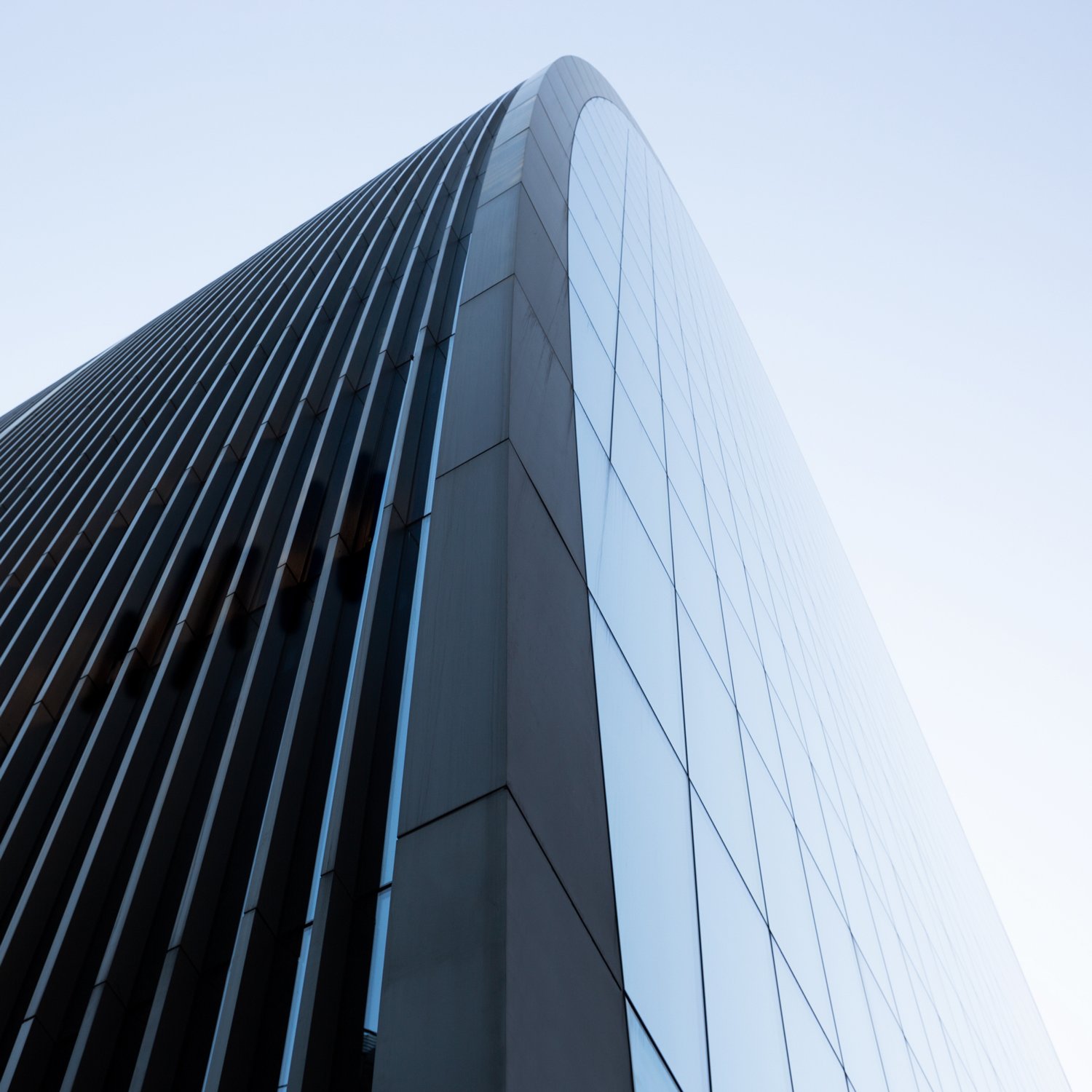 Blue glass skyscraper photographed from below, rising to a curved pointed roofline.