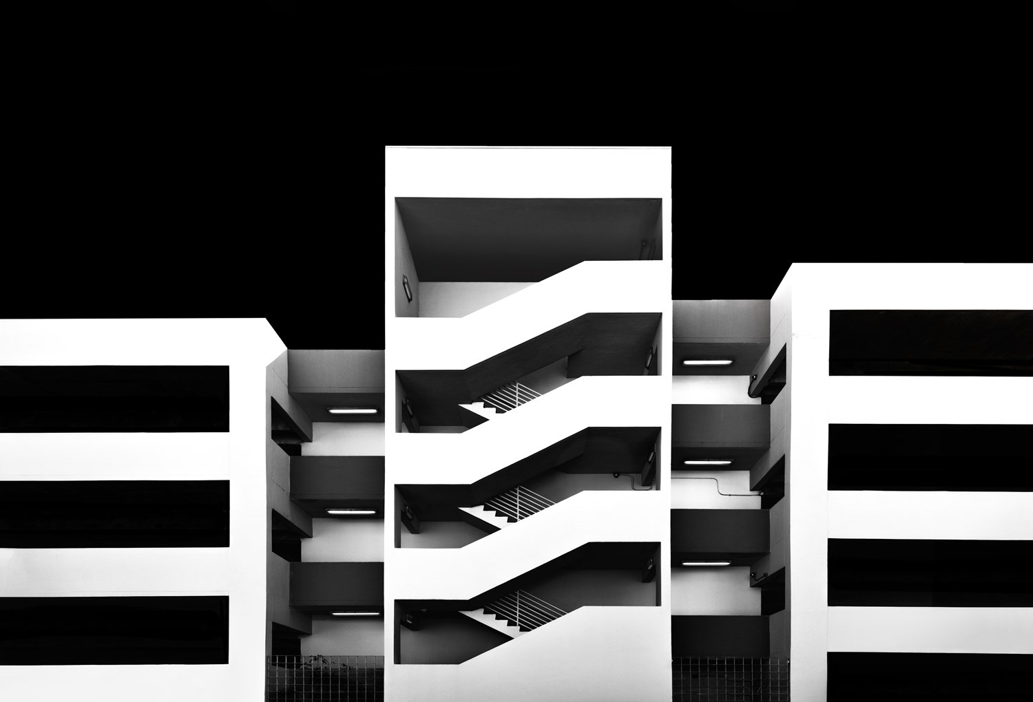 Black-and-white modernist facade with repeating geometric balconies of a car park.