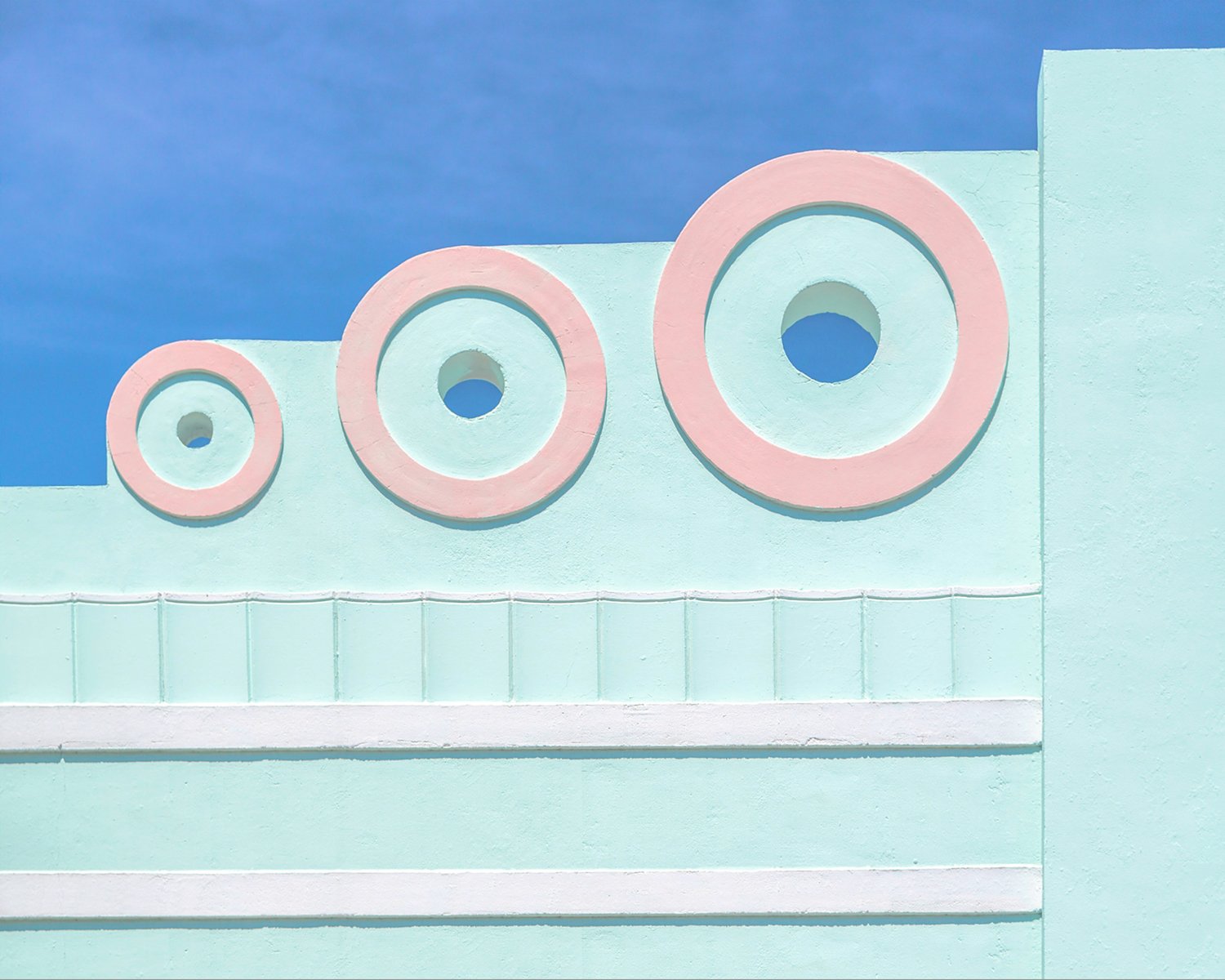 Mint-green Art Deco facade with three pink circular motifs against blue sky.