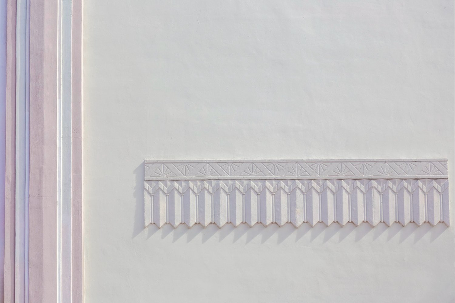 White wall with a repeating decorative relief casting delicate shadows.