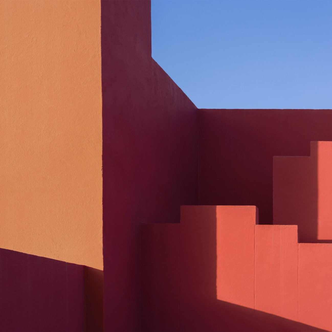 Orange and deep red geometric walls framing a patch of blue sky.