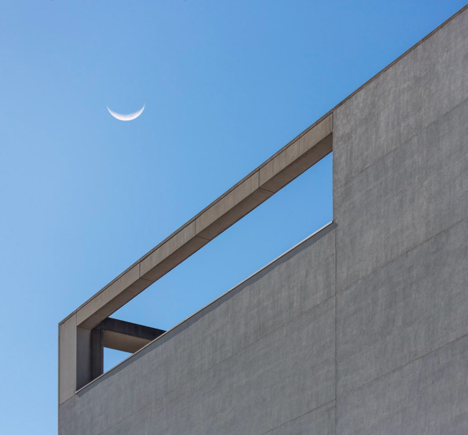 Crescent moon above a diagonal concrete beam and pale blue sky.
