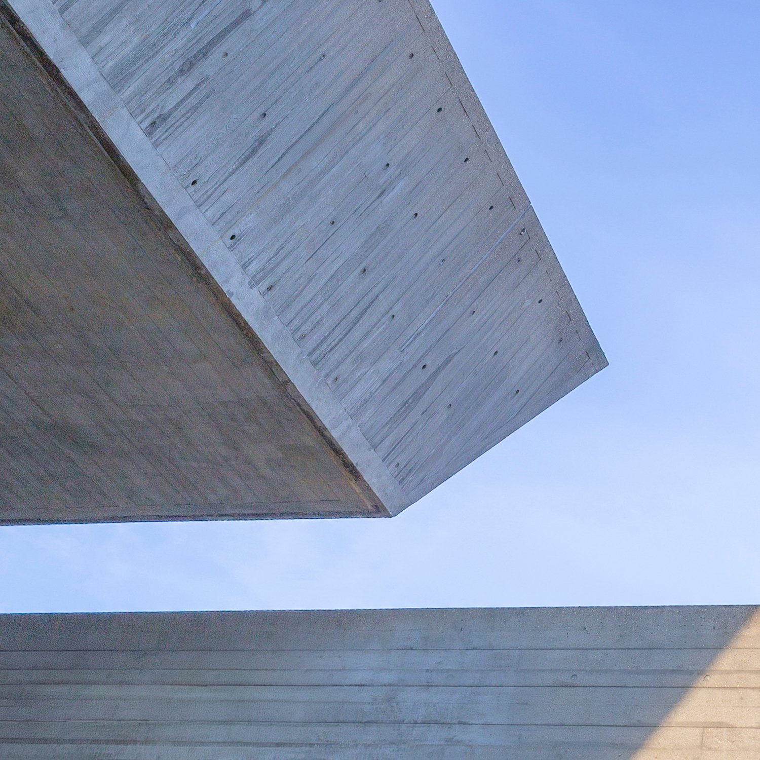 Angled concrete planes forming a minimalist composition against a blue sky.