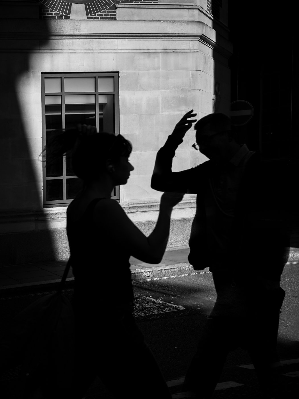 Two people in silhouette gesturing against a bright building facade.