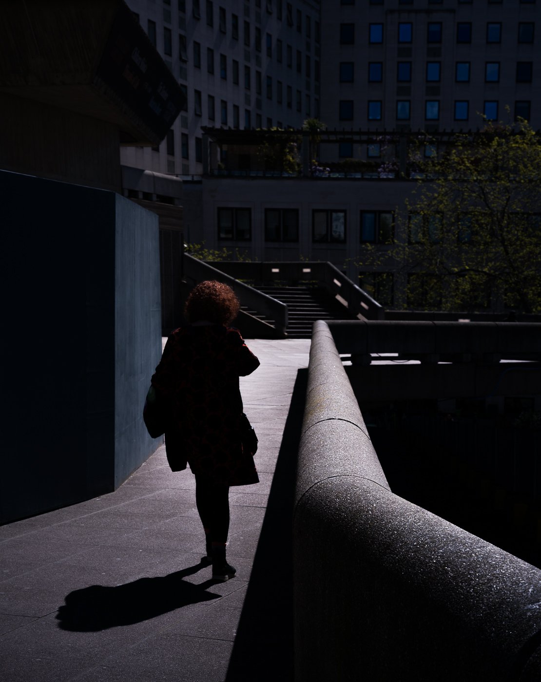 Person walking beside a curving concrete wall in strong light and shadow.