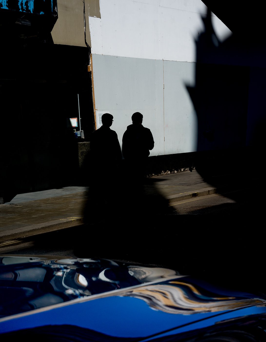 Two silhouetted figures standing against a large bright wall.