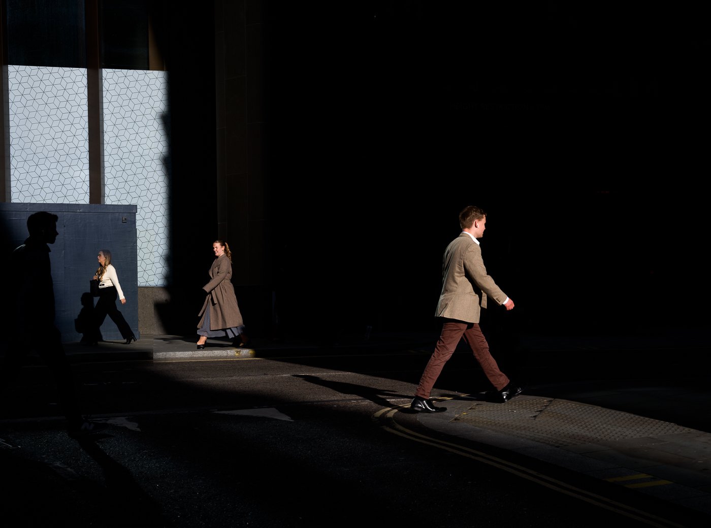 Man crossing a narrow strip of sunlight with other pedestrians in the darker background.