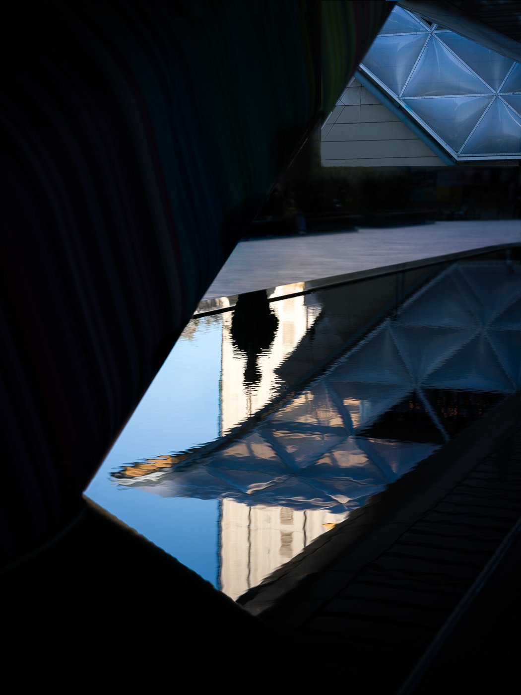 Reflected figure and angular modern architecture in a dark glossy surface.