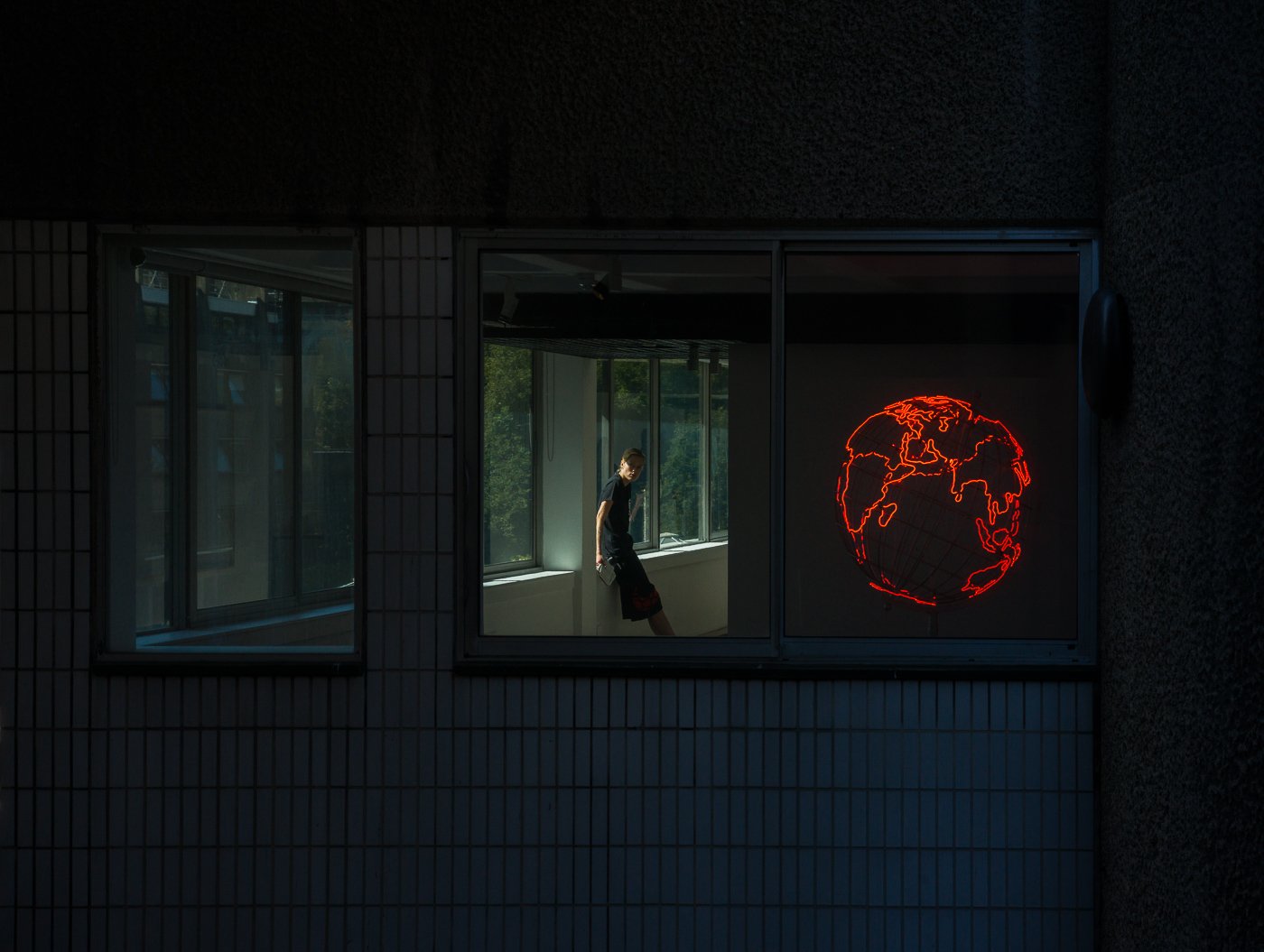 Person framed in a lit window beside a red neon globe sign.