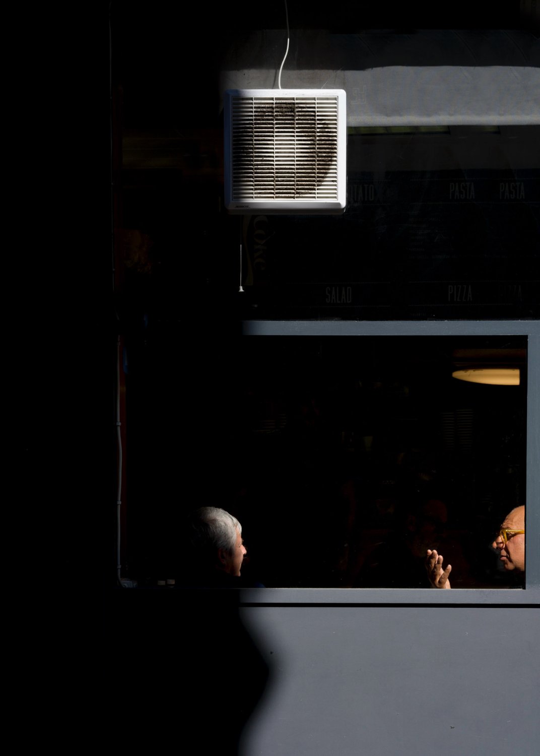 People partly silhouetted in a dark interior beneath rectangular ceiling lights.