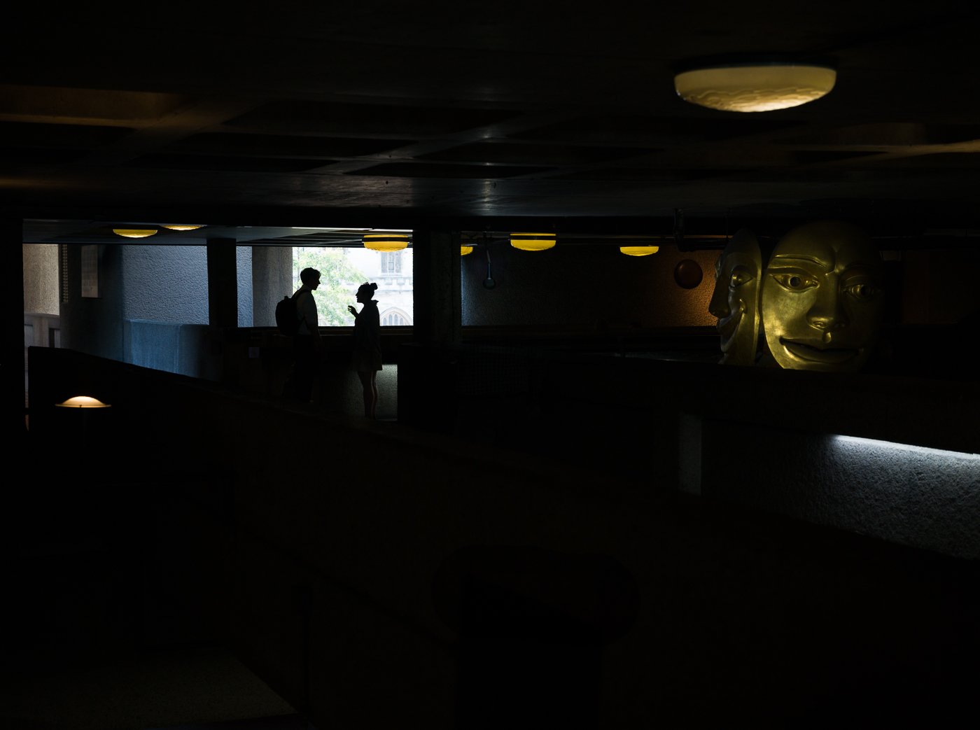 Silhouetted figures in a dark interior with an illuminated sculptural face.